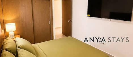 A hotel room with a bed, a TV mounted on the wall, and a wardrobe.