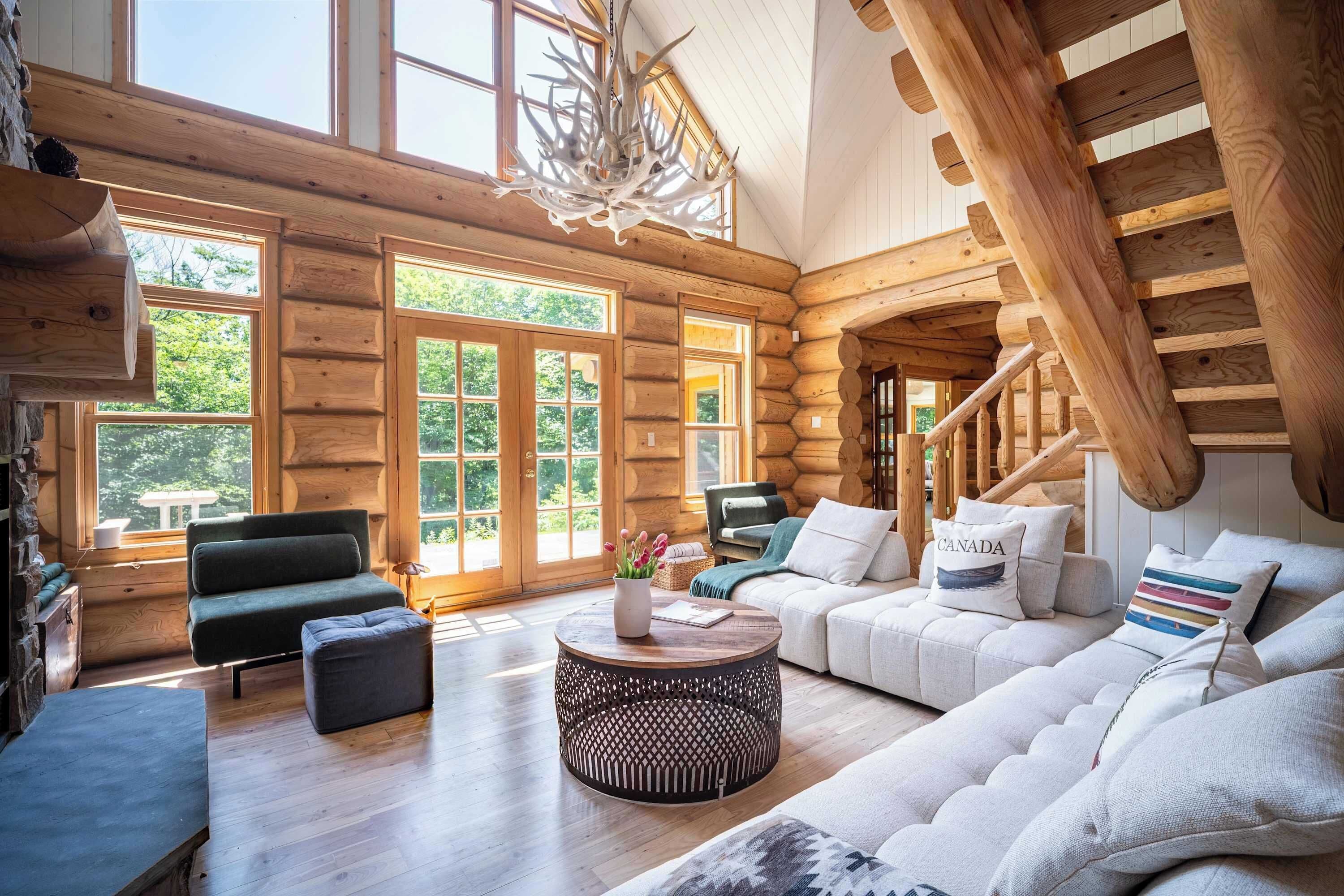 L’intérieur d’une cabane en rondins, avec un escalier en bois, un ensemble de canapés et une table à manger.