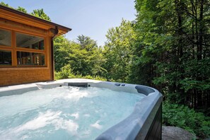 Ein Whirlpool inmitten von Bäumen, im Hintergrund ein Holzhaus.