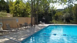 Ein Schwimmbecken mit Holzterrasse, Liegestühlen und einem umzäunten Bereich.