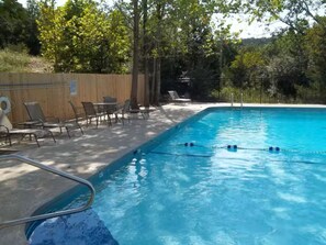 Ein Schwimmbecken mit Holzterrasse, Liegestühlen und einem umzäunten Bereich.