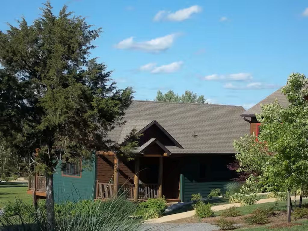 Un chalet doté d’un porche couvert et d’une petite terrasse, entouré d’arbres et bordé d’une pelouse bien entretenue.
