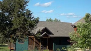 Eine Lodge mit überdachter Veranda und einer kleinen Terrasse, umgeben von Bäumen und einem gepflegten Rasen.
