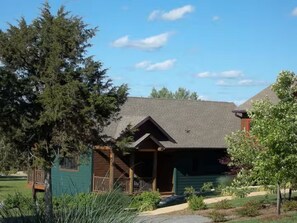 Eine Lodge mit überdachter Veranda und einer kleinen Terrasse, umgeben von Bäumen und einem gepflegten Rasen.