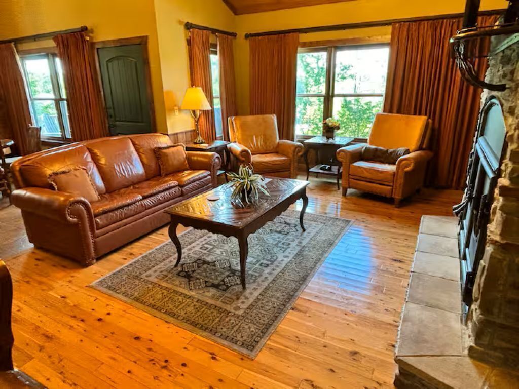 A cozy living room with a brown leather sofa, two armchairs, a coffee table, and a fireplace.