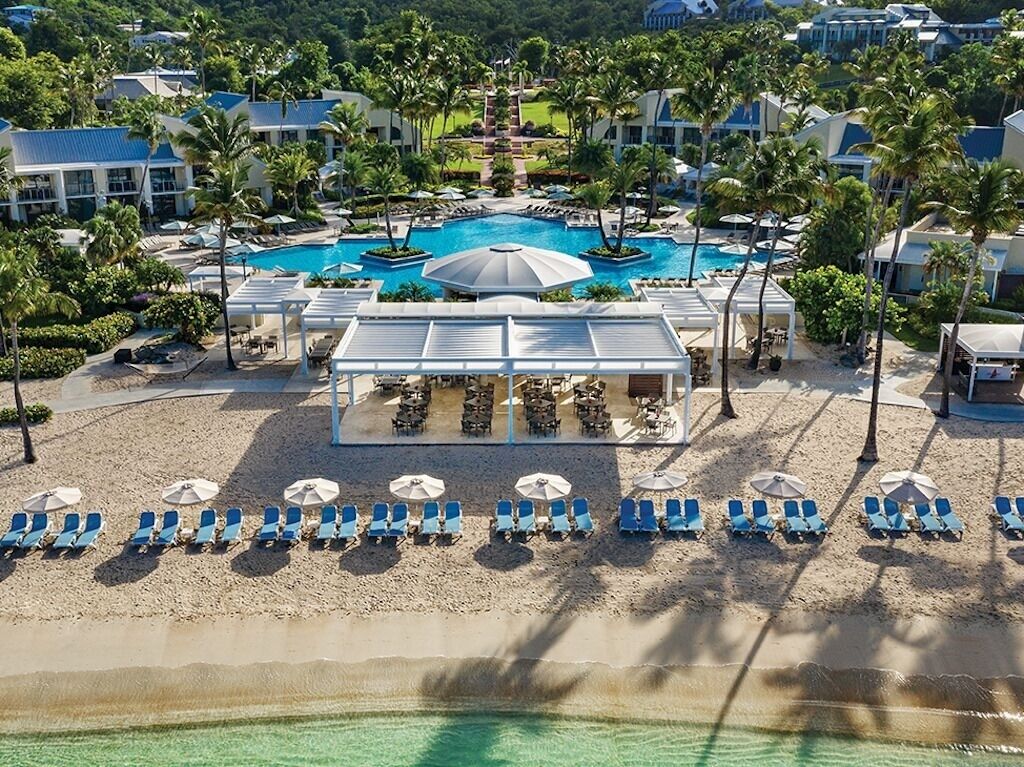 Un resort con piscina, sillas de playa, sombrillas y palmeras.