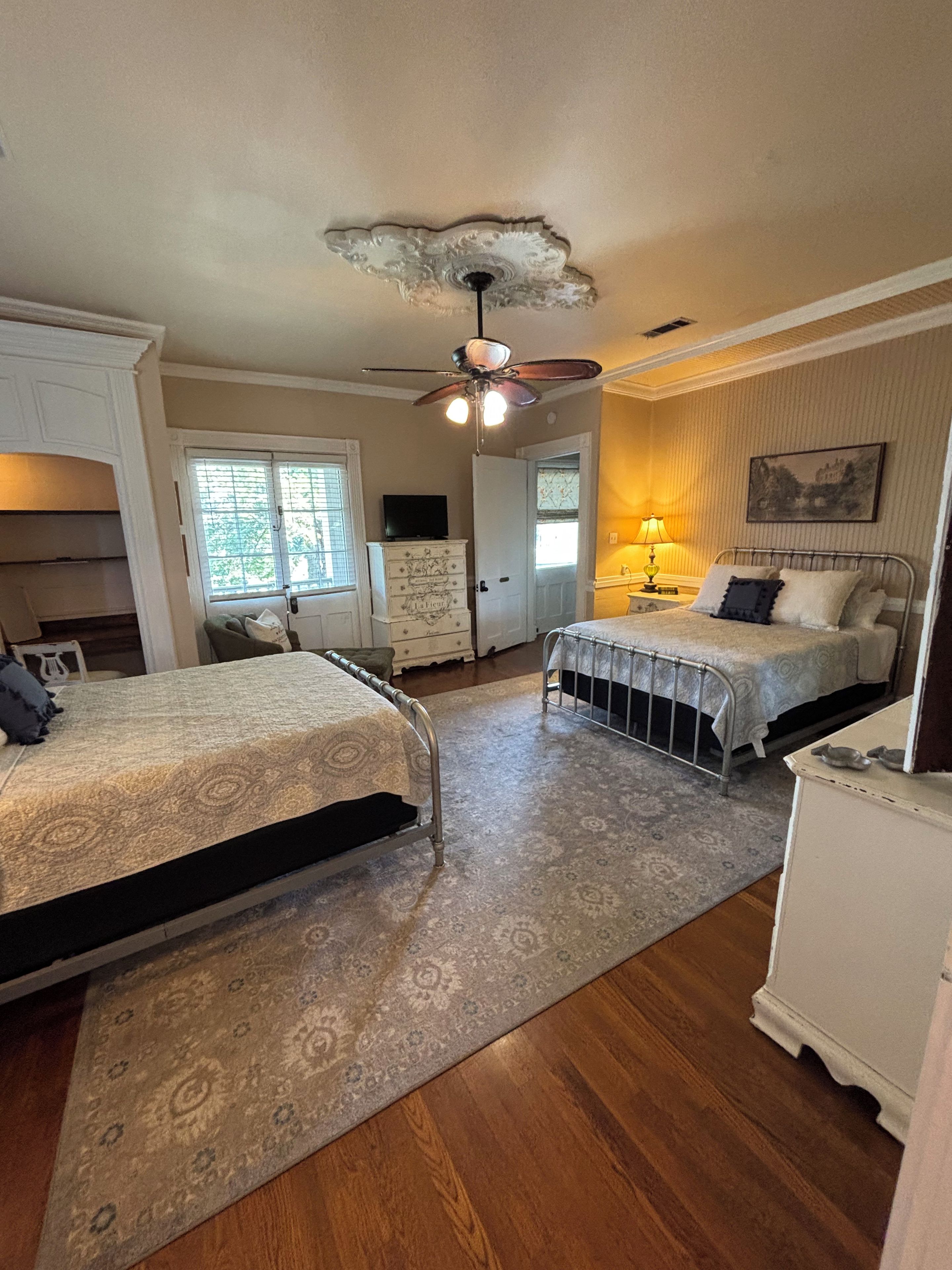 A bedroom with two beds, a ceiling fan, a dresser, a lamp, and a window.