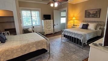 A bedroom with two beds, a ceiling fan, a dresser, a lamp, and a window.