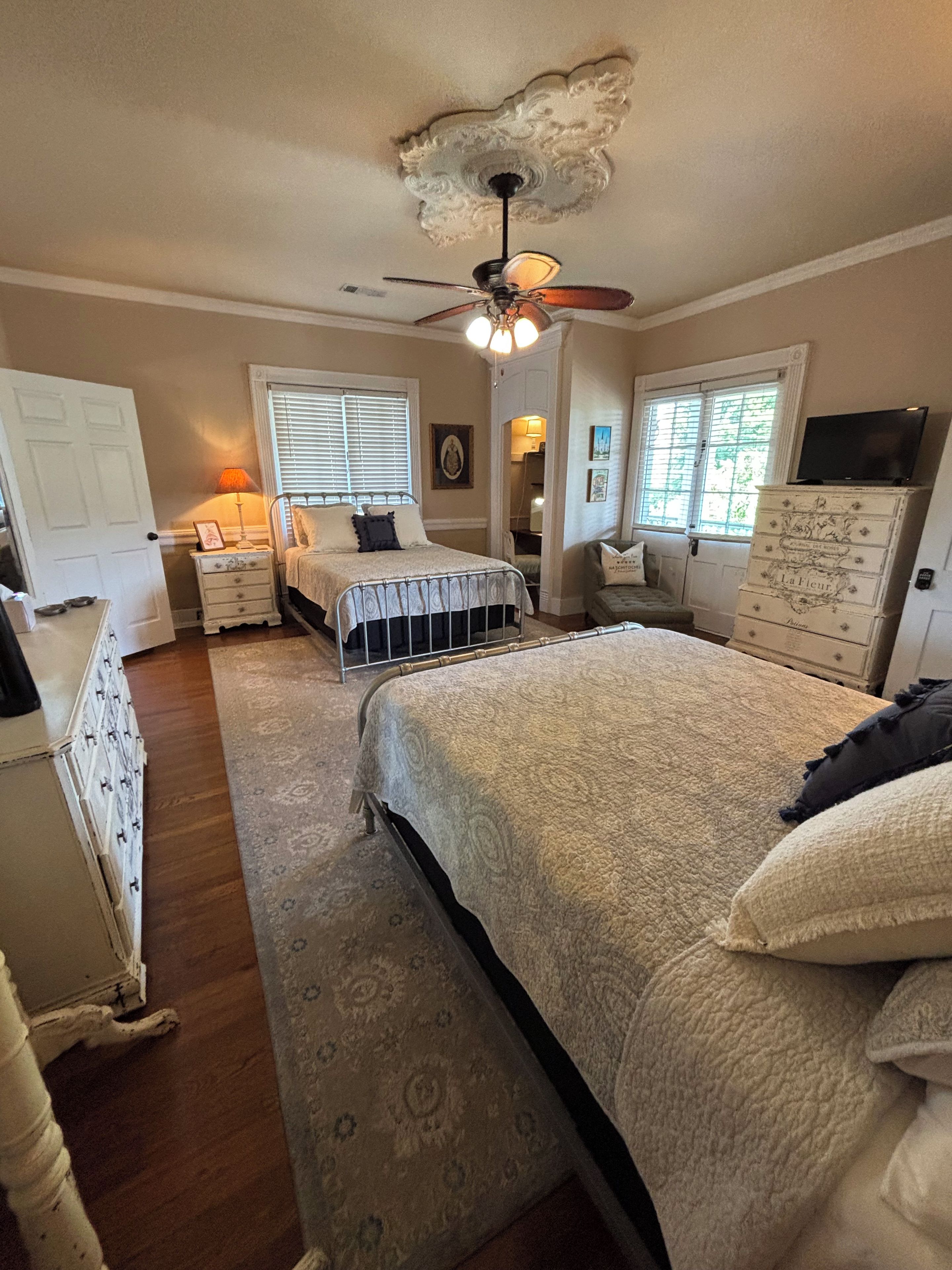 A bedroom with a large bed, a ceiling fan, a dresser, and a television on a cabinet.