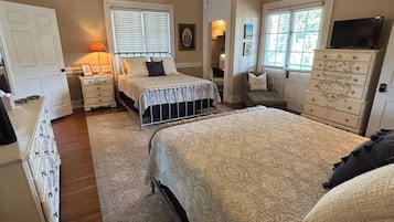A bedroom with a large bed, a ceiling fan, a dresser, and a television on a cabinet.