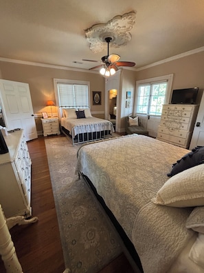 A bedroom with a large bed, a ceiling fan, a dresser, and a television on a cabinet.