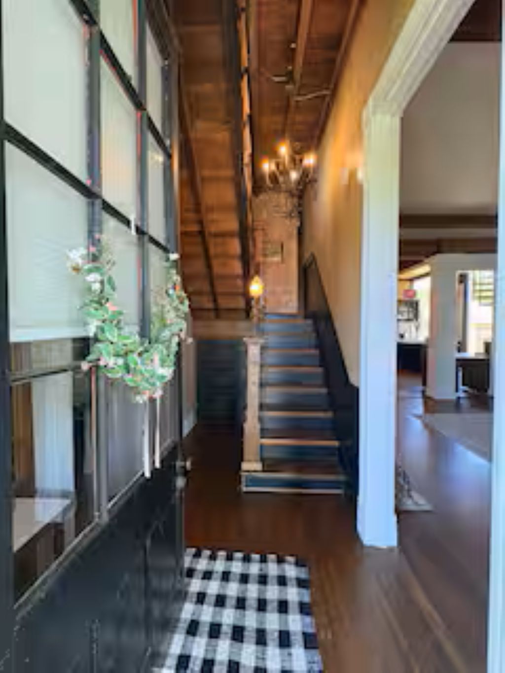 Un pasillo con un tapete de cuadros, escaleras de madera y una escalera que sube a otro nivel.