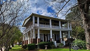 A two-story house with a porch, surrounded by trees and a well-maintained lawn.