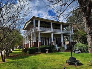 A two-story house with a porch, surrounded by trees and a well-maintained lawn. - The Steamboat House, Captain's Quarters-Bed & Breakfast Style Experience (Natchitoches)
