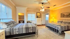A bedroom with a large bed, a ceiling fan, and a window with blinds.