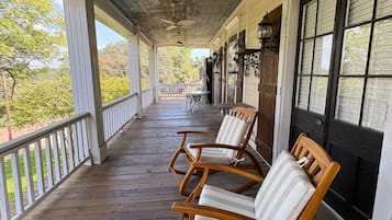 A covered porch with wooden flooring, ceiling fans, and outdoor seating with cushioned chairs.
