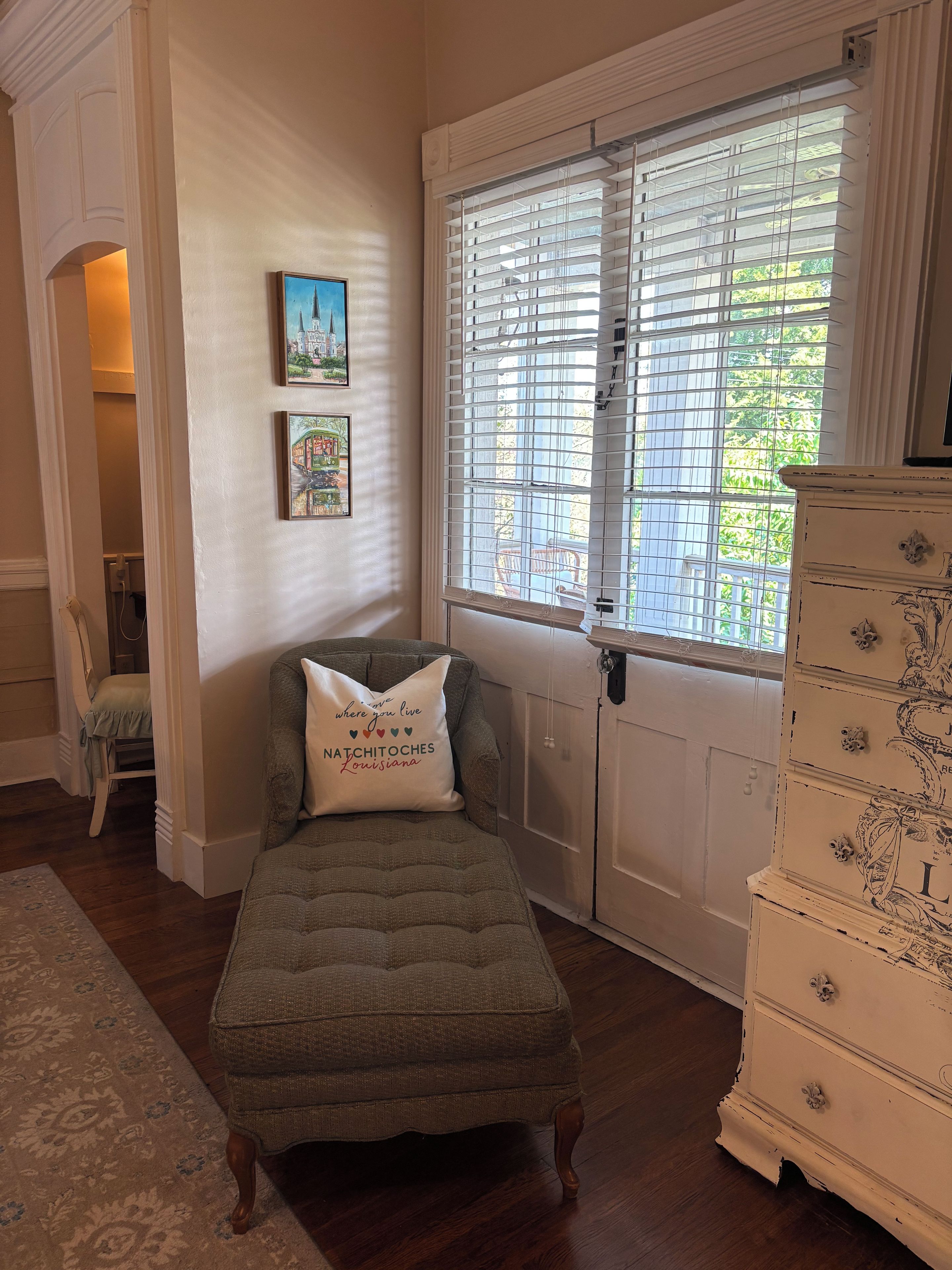 A room with a single green upholstered bench, a white dresser with ornate handles, and two framed pictures on the wall.