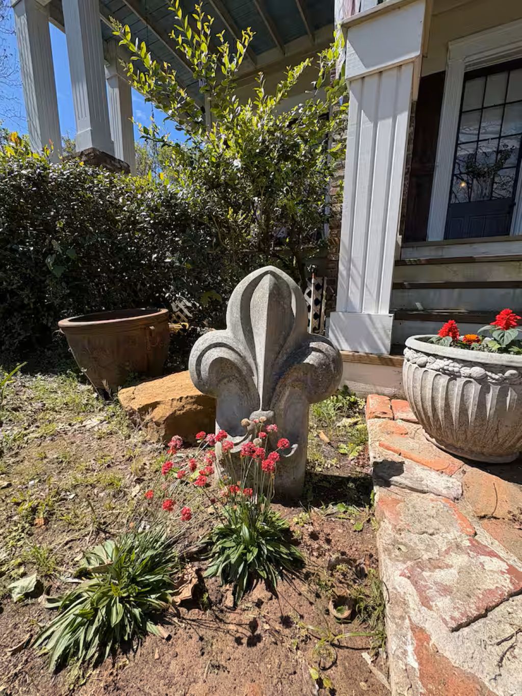 A garden with a stone fountain, potted plants, and a building with columns.