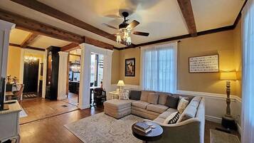A spacious living room with a large sectional sofa, a round coffee table, and a ceiling fan. There is a dining area visible in the background.