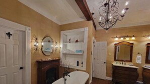 A bathroom with a freestanding bathtub, a vanity with a mirror, and a chandelier.