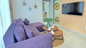 A living room with a purple sofa, a round coffee table, a ceiling fan, and a flat-screen TV mounted on a wooden panel wall. - ANYA 5 Chic Coastal Oasis • King Bed & Balcony (Bayahíbe)