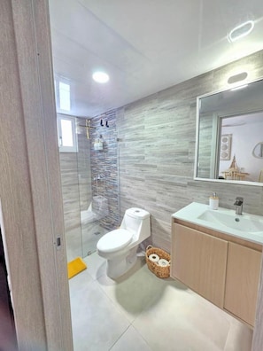A modern bathroom with a glass shower enclosure, a toilet, a sink with a mirror, and a wooden vanity. - ANYA 5  Caribbean Apartment 1BR APT Pool view (Bayahíbe)