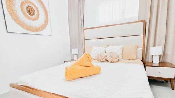 A bedroom with a large bed, a bedside table, a wall-mounted lamp, and a ceiling light fixture. - ANYA 5 Chic Coastal Oasis • King Bed & Balcony (Bayahíbe)