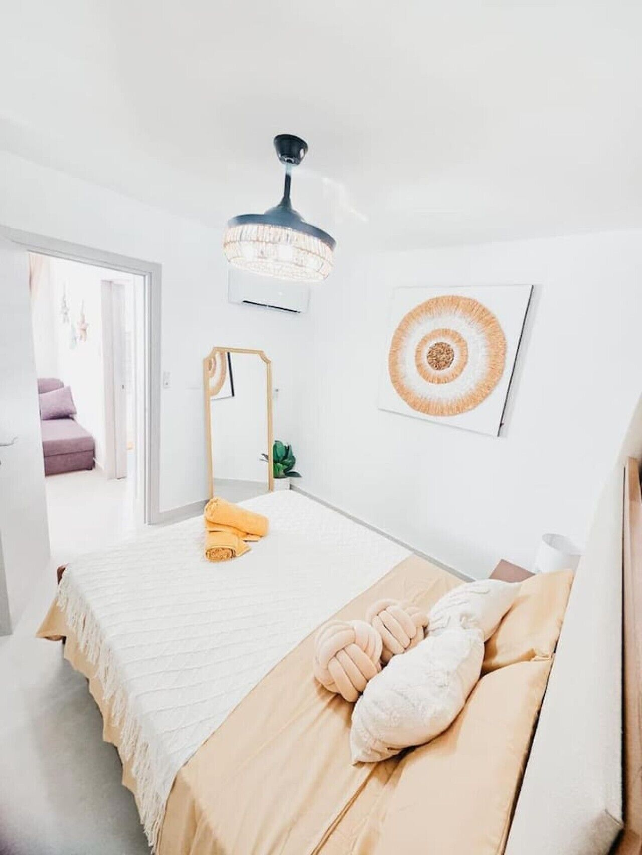 Un dormitorio minimalista con cama, lámpara de noche, aire acondicionado de pared y una obra de arte enmarcada.