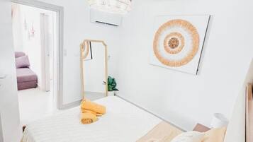 Un dormitorio minimalista con cama, lámpara de noche, aire acondicionado de pared y una obra de arte enmarcada.