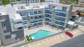 A multi-story hotel with a swimming pool and a red car parked nearby. - ANYA 5 Chic Coastal Oasis • King Bed & Balcony (Bayahíbe)