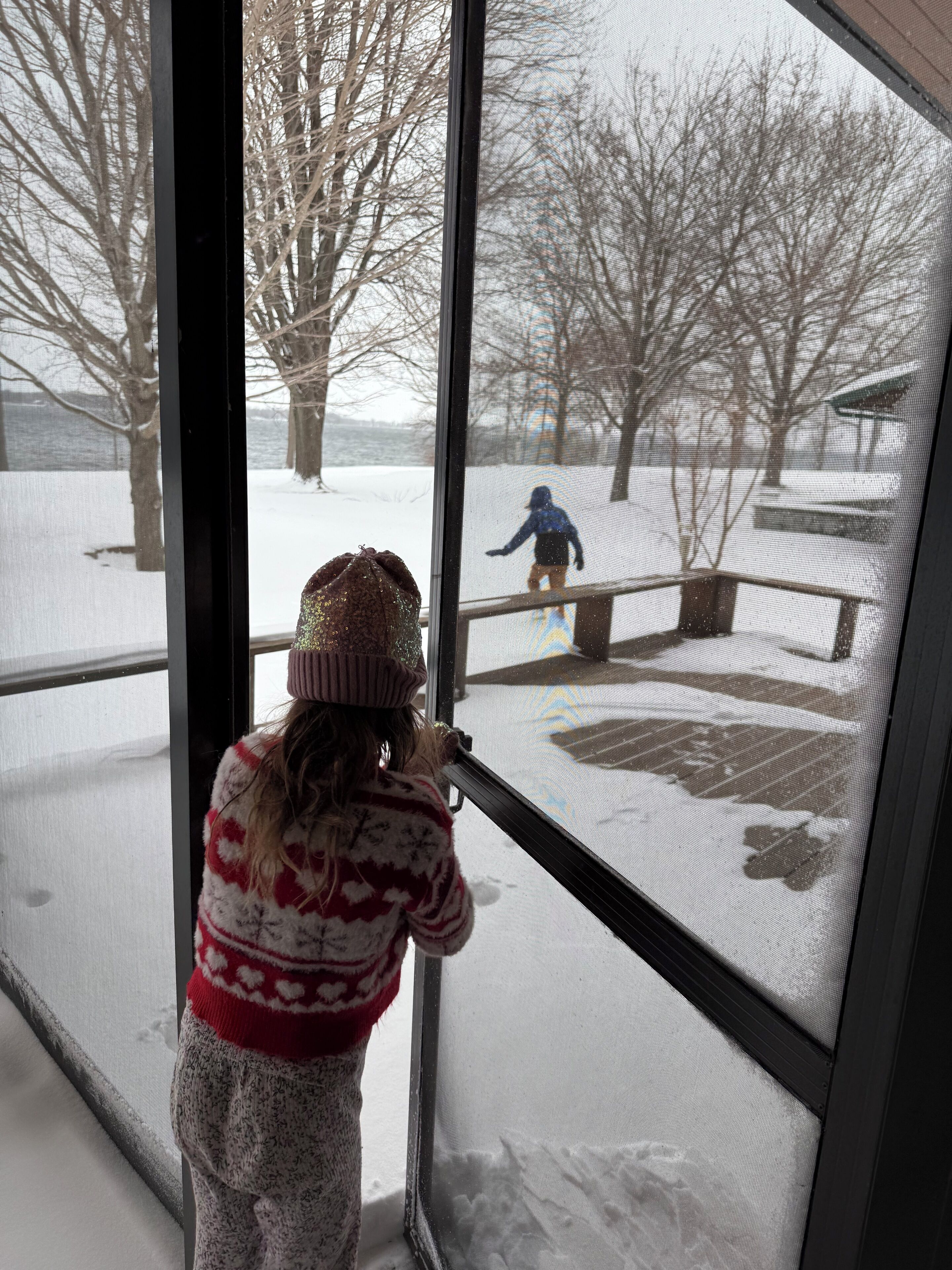 A child looking out a window at a snowy outdoor scene.