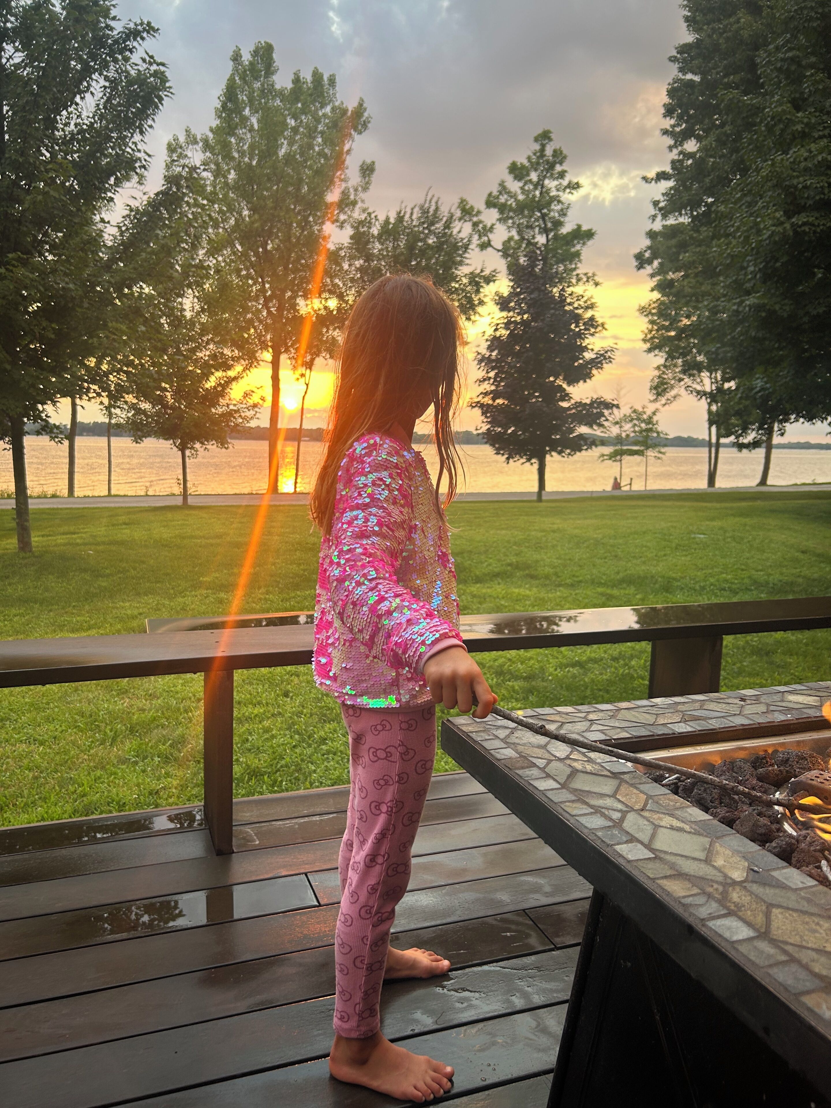 A child standing on a wooden deck overlooking a body of water with trees in the background.