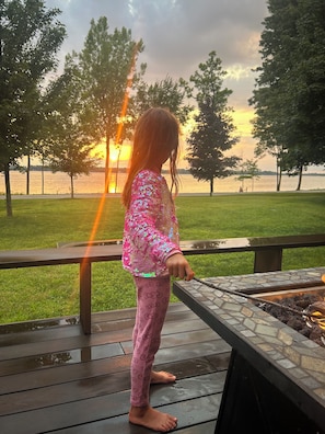 A child standing on a wooden deck overlooking a body of water with trees in the background.