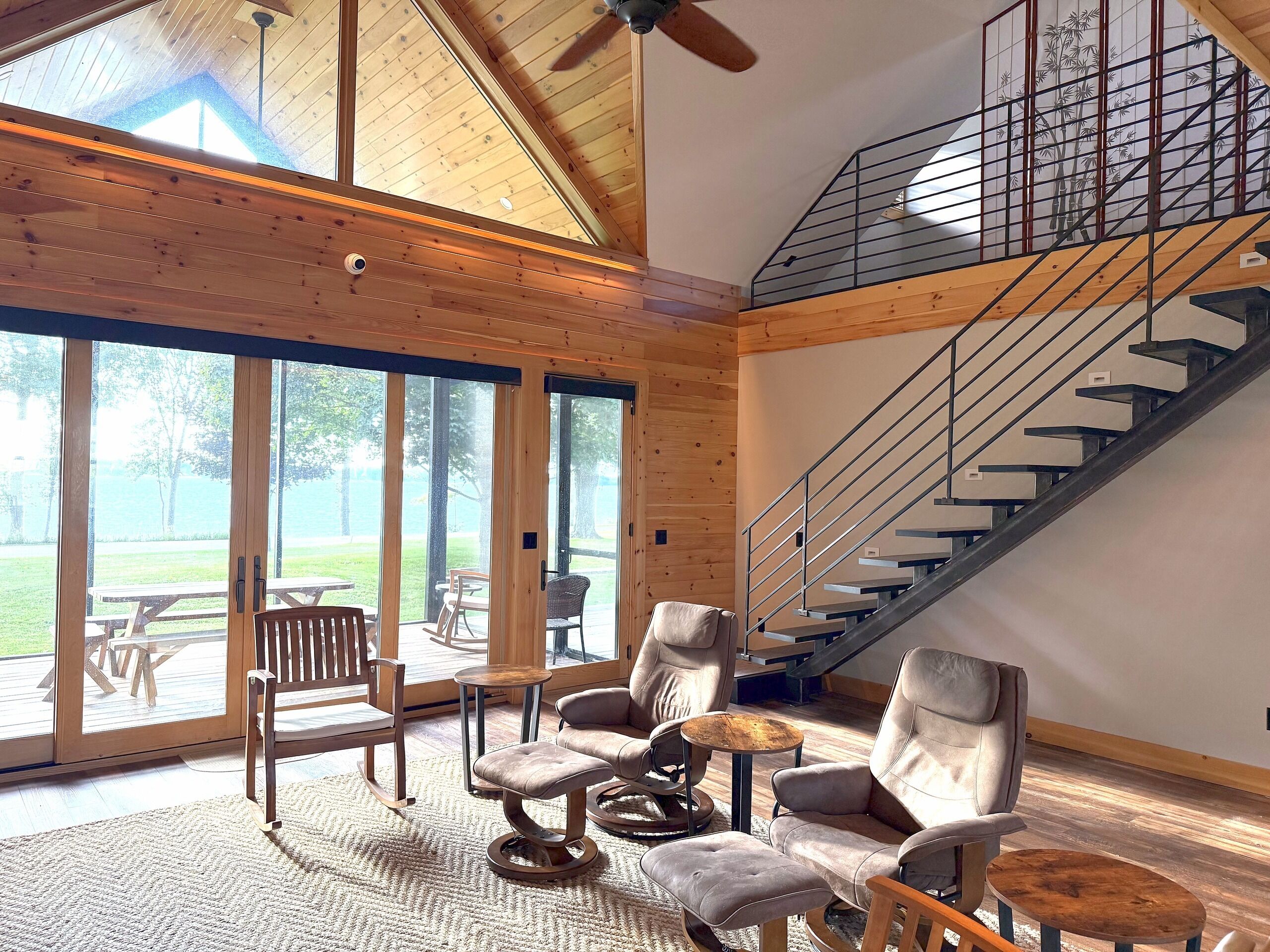 A spacious room with a high ceiling, a wooden staircase, and a view of the outdoors.