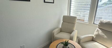 A living room with a beige sofa, a wooden coffee table with a plant, and two framed botanical prints on the wall.