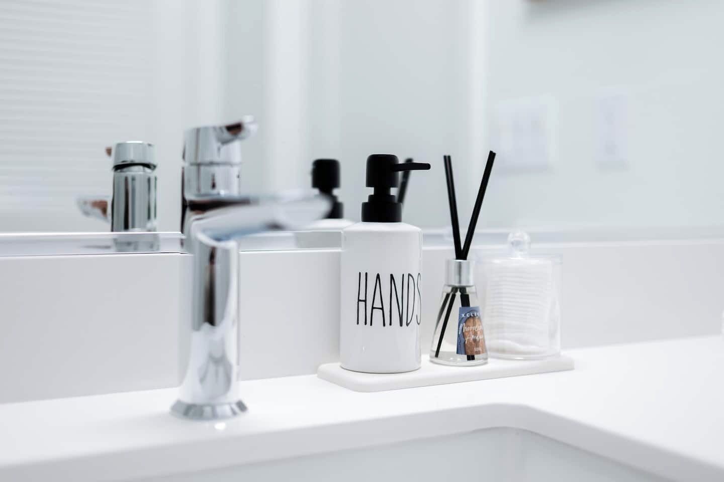 Un bagno con un lavandino bianco, un dispenser di sapone, un contenitore per sapone mani e una bottiglia di disinfettante per le mani.