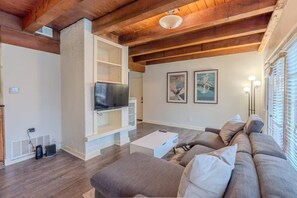 Ein Wohnzimmer mit Holzboden, einem Flachbildfernseher, einer Couch und zwei gerahmten Bildern an der Wand.