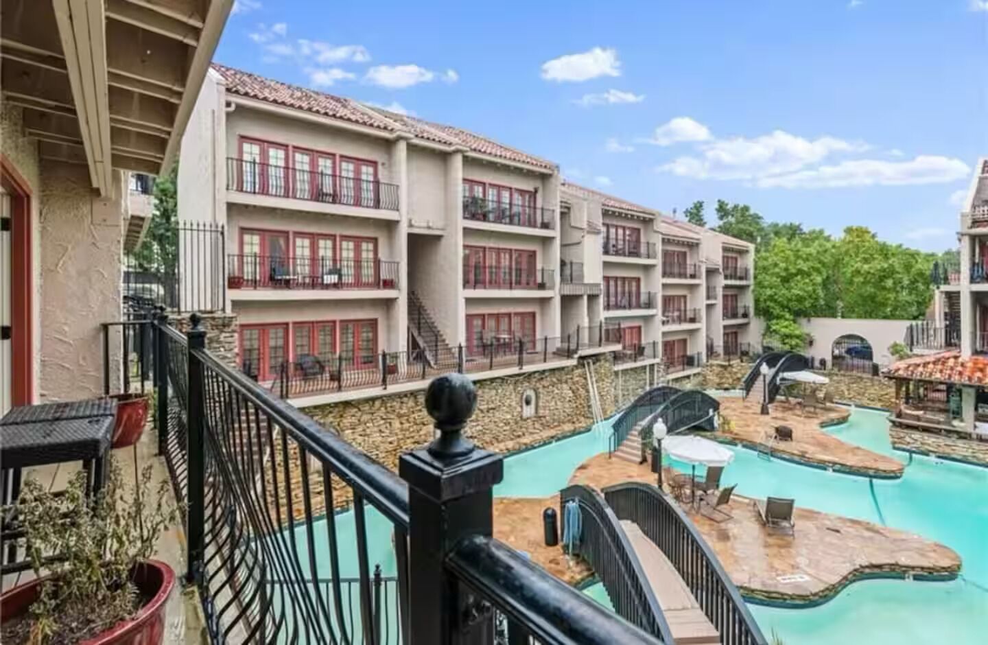 Un hotel con varios balcones, piscina y un muro de piedra.
