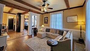 A spacious living room with a large sectional sofa, a round coffee table, and a ceiling fan. There is a dining area visible in the background.