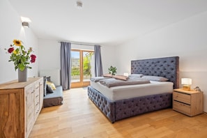 A bedroom with a large bed, a wooden dresser, a nightstand, and a window with curtains. - Spacious vacation rental with mountain views and a terrace near the highway and Lake Simssee (Rohrdorf)