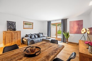A modern living room with a wooden dining table, a grey sofa, and a wooden cabinet. - Spacious vacation rental with mountain views and a terrace near the highway and Lake Simssee (Rohrdorf)