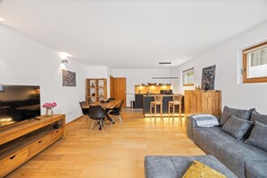 A modern living room with a flat-screen TV, a grey sofa, and a wooden dining table with chairs. - Spacious vacation rental with mountain views and a terrace near the highway and Lake Simssee (Rohrdorf)