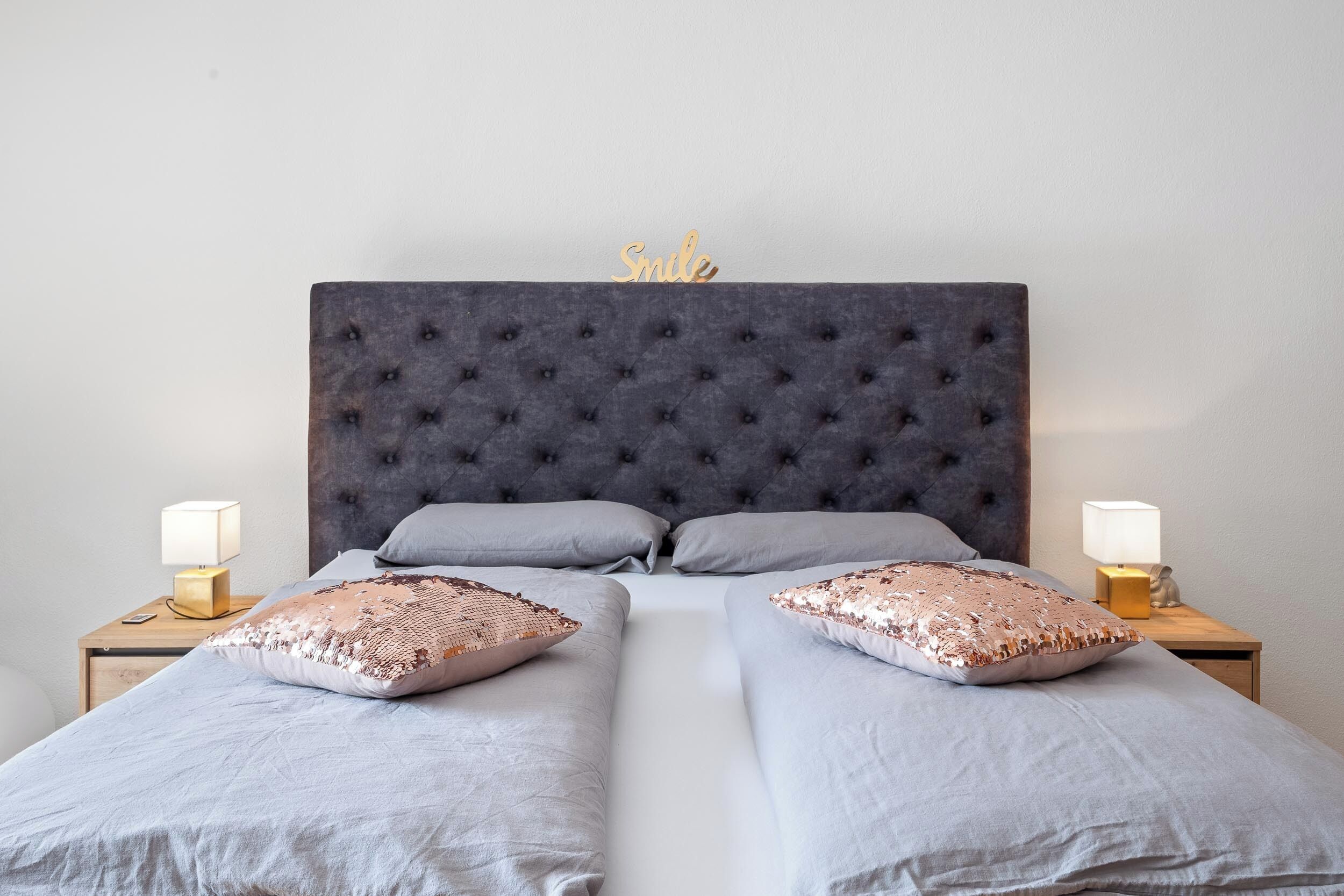A double bed with a tufted headboard, two bedside tables with lamps, and decorative pillows.