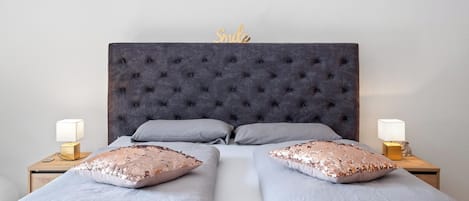 A double bed with a tufted headboard, two bedside tables with lamps, and decorative pillows.