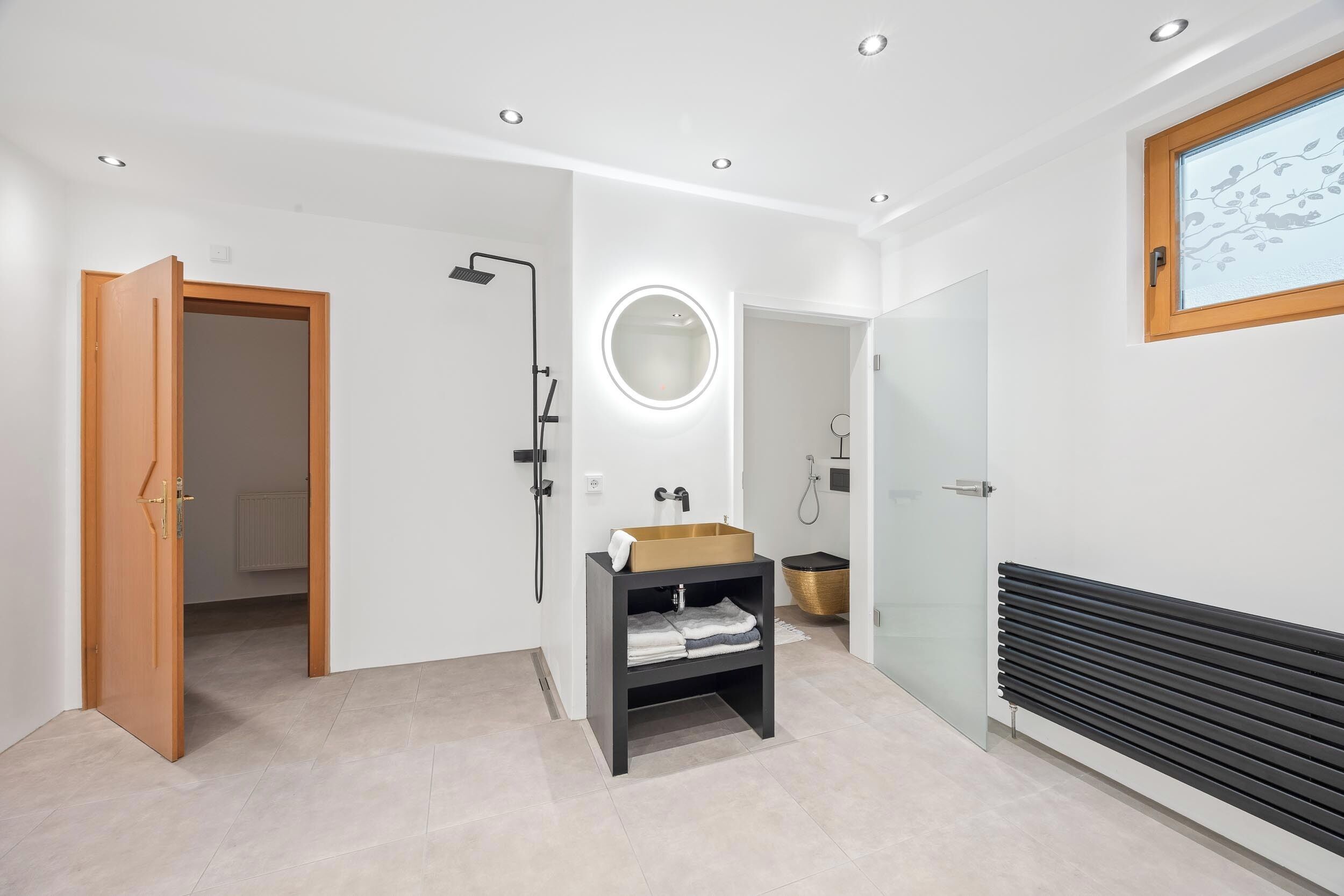 A modern bathroom with a glass shower enclosure, a vanity with a gold basin, and a radiator.