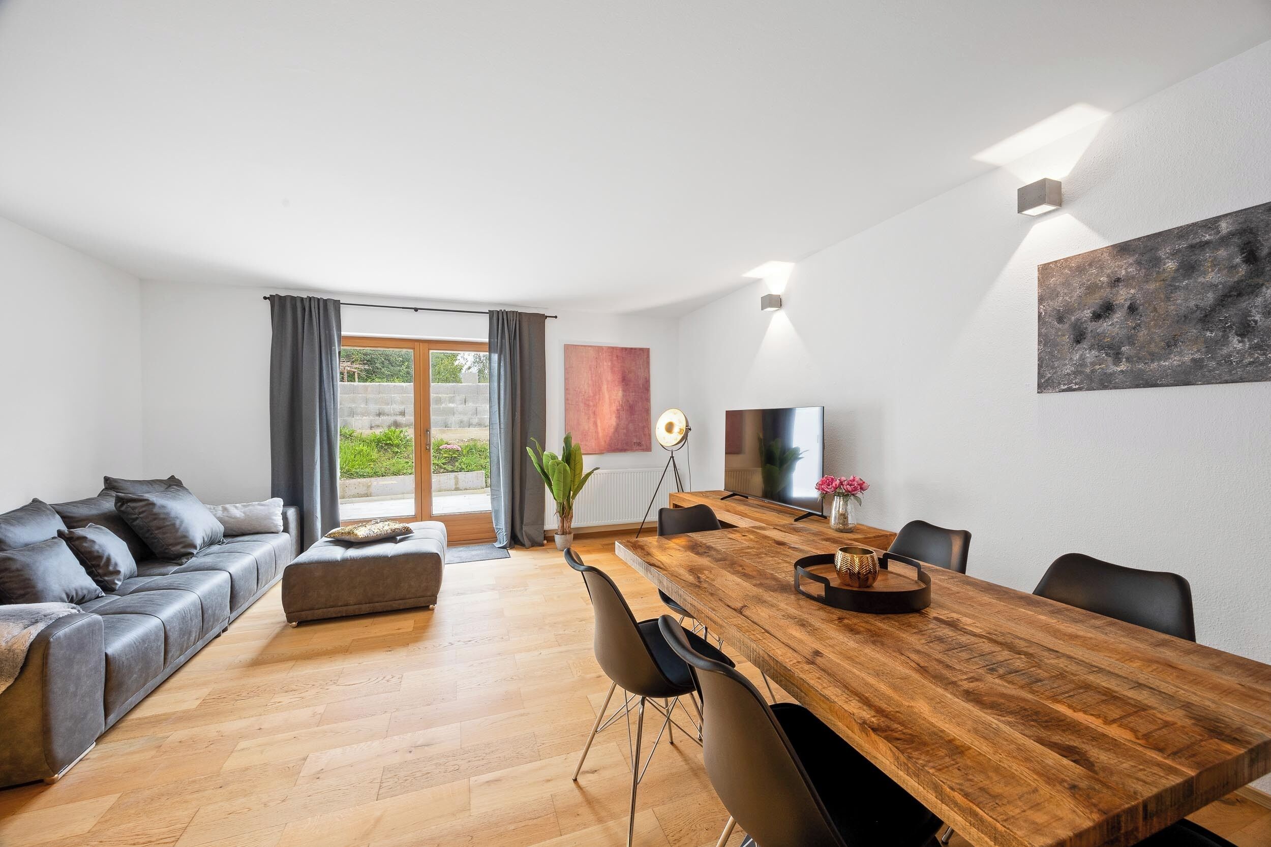 Ein modernes Wohnzimmer mit einem Holzesstisch, einem grauen Sofa und einem Fernseher.