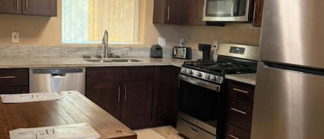 A kitchen with dark wooden cabinets, stainless steel appliances, a window with blinds, and a table with a placemat.
