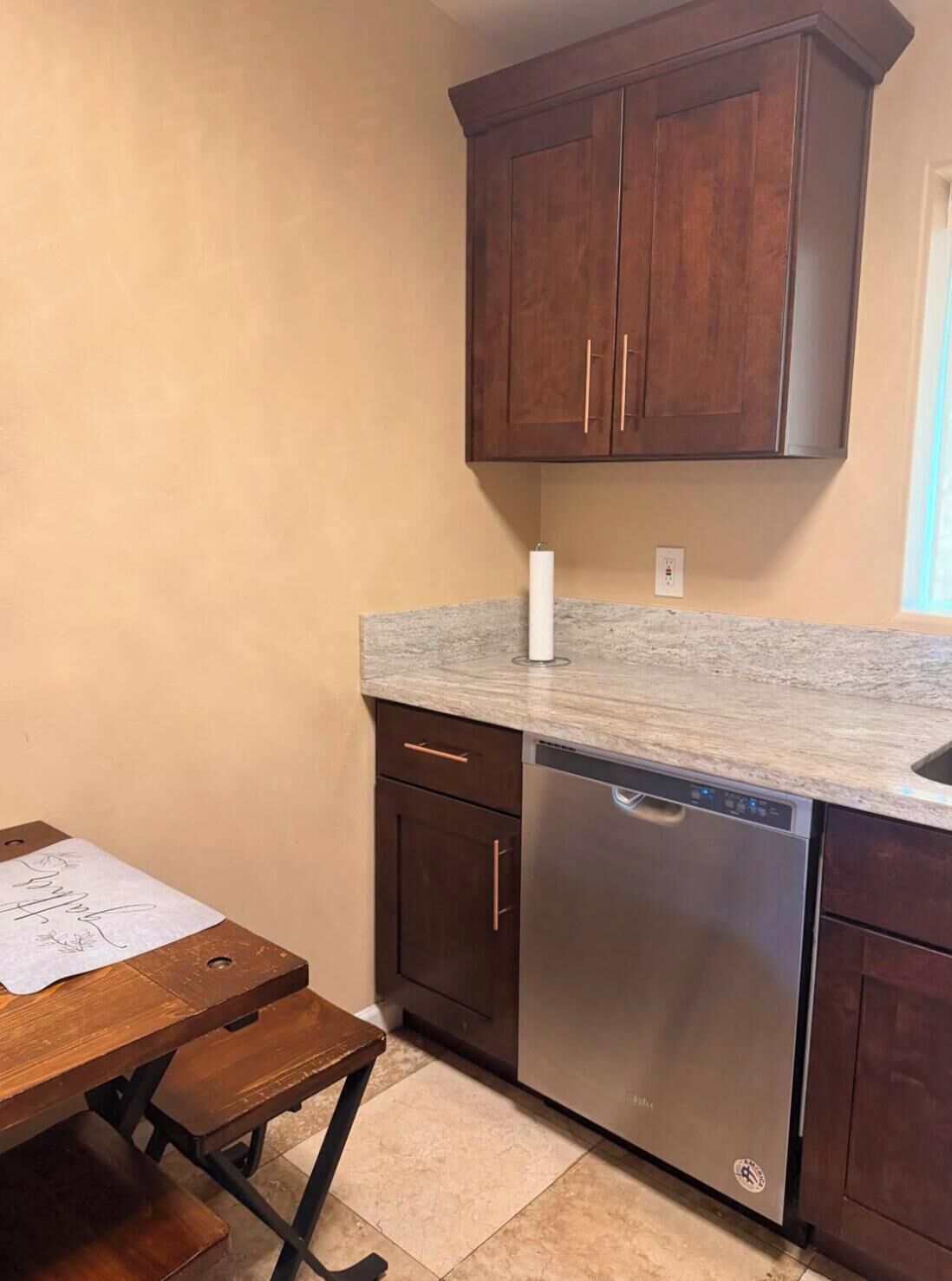 A kitchen with wooden cabinets, a stainless steel dishwasher, and a marble countertop.
