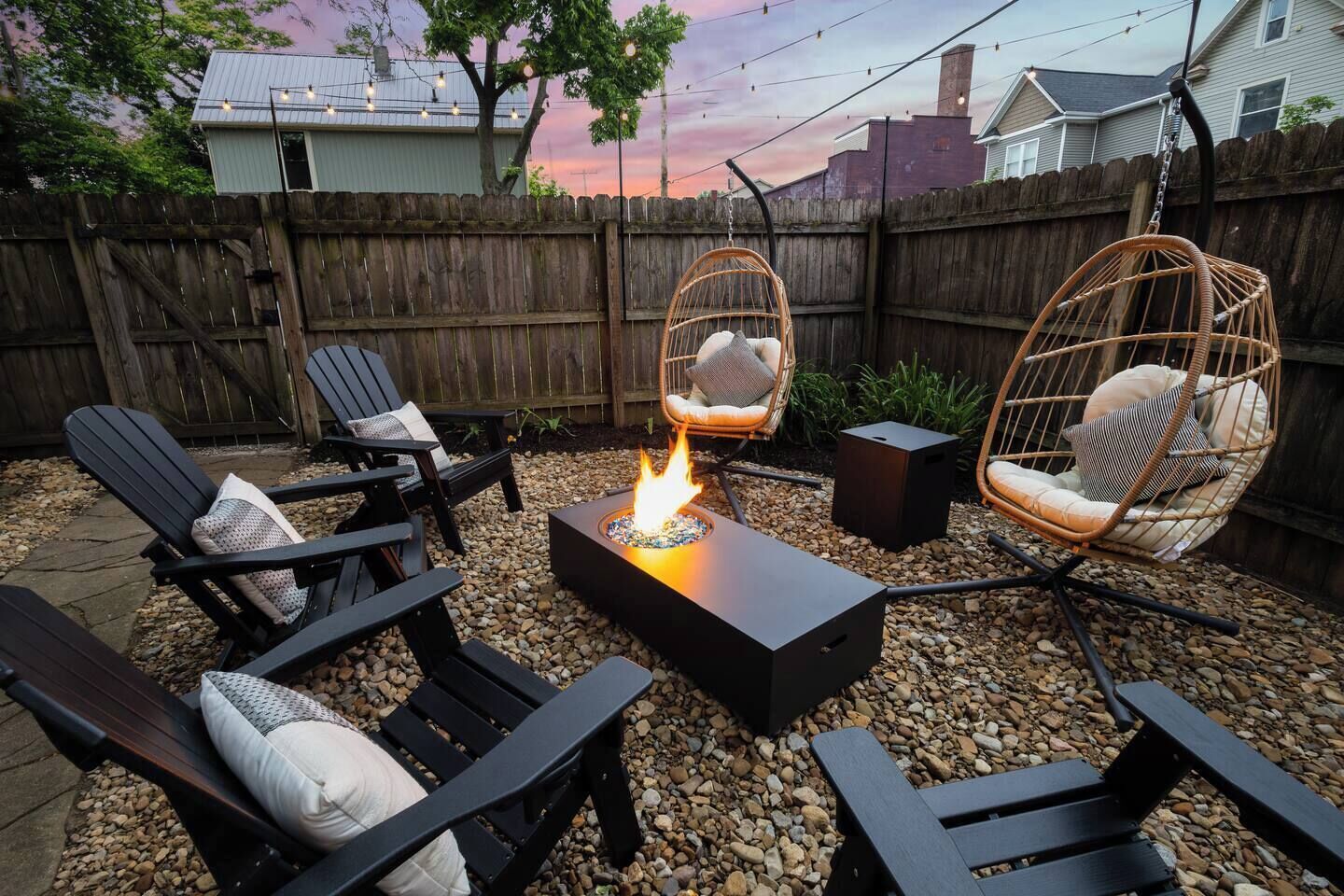 Een terras met een vuurkuil, zwarte stoelen en rieten stoelen.
