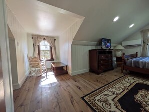 A bedroom with a wooden floor, a bed, a dresser, a television, and a window with curtains. - Gingerbread Home | Quiet Stay | 30+ Day Ready (Chattanooga)